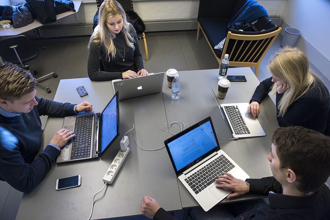 Fire studerende fra Aalborg Universitet arbejder ved hver sin computer omkring et gruppebord
